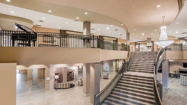 A spacious hotel lobby with a grand staircase, multiple seating areas, and a chandelier.