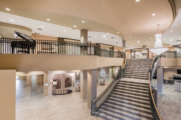 A spacious hotel lobby with a grand staircase, multiple seating areas, and a chandelier.