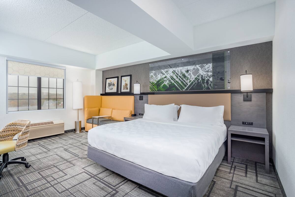 A hotel room with a large bed, a desk, a chair, and a window with a view.