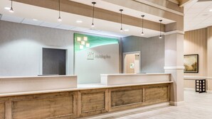 A reception area with a modern design, featuring a reception desk, a wall-mounted information board, and a wooden panel accent.