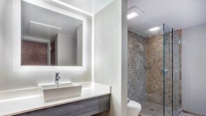Une salle de bain moderne avec un grand miroir, un lavabo blanc et une douche à parois de verre.
