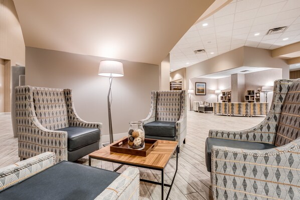 A modern lobby with patterned armchairs, a wooden coffee table, and a floor lamp. - Holiday Inn Lafayette-City Centre by IHG (Lafayette)