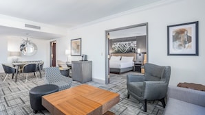 A hotel room with a bed, a desk, a chair, a sofa, and a dining table.