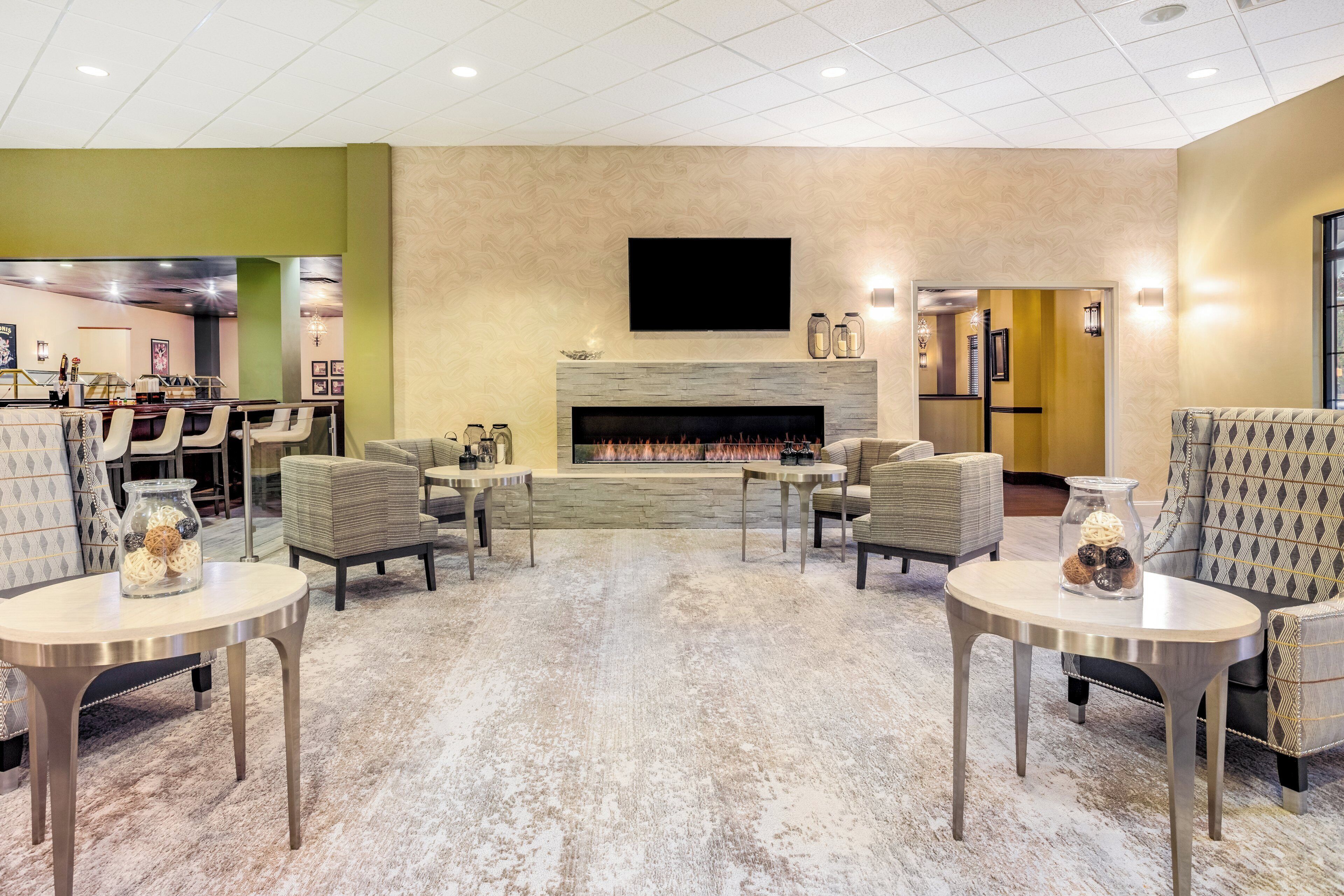 A modern lounge area with a fireplace, seating, and a flat-screen TV mounted on the wall.