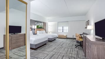 A hotel room with a large mirror, two beds, a desk, a TV, and a window with blinds.