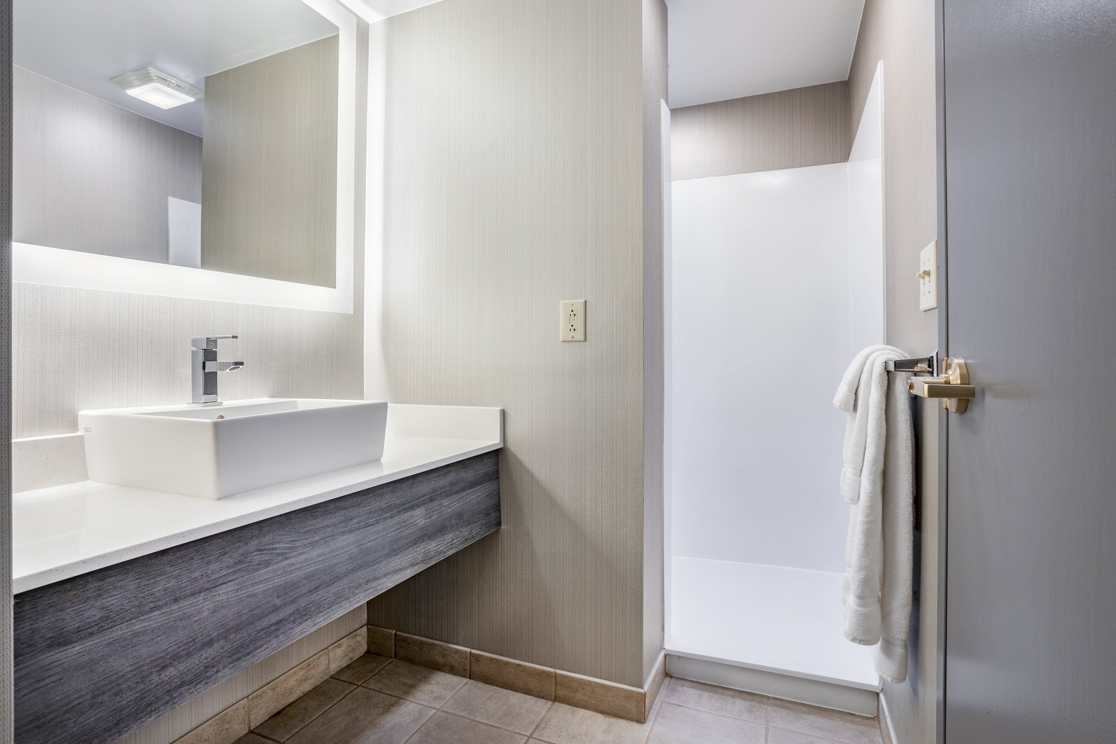 A modern bathroom with a large mirror, a white sink, and a shower area.