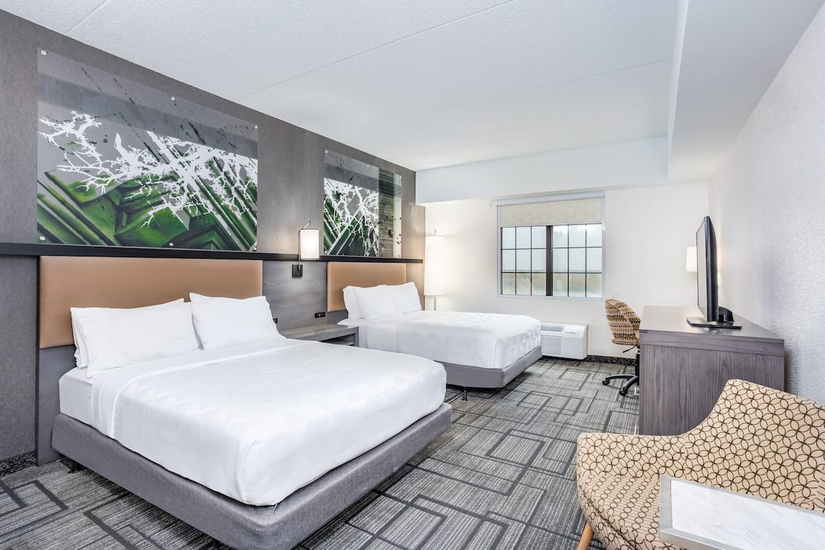 A hotel room with two beds, a desk, a chair, and a large abstract painting on the wall.