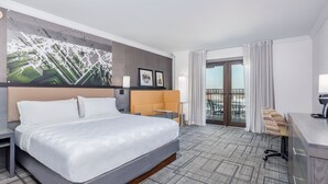 Une chambre d’hôtel avec un grand lit, un bureau, une chaise, un balcon et une œuvre d’art représentant un paysage urbain accrochée au mur.