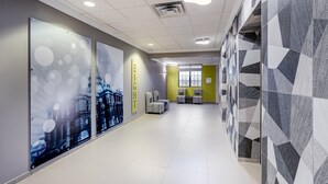 Un couloir moderne aux murs ornés de motifs, avec un espace détente comprenant des fauteuils et une grande fenêtre laissant entrer la lumière.