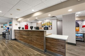 A hotel reception area with a wooden reception desk, a digital screen, and a coffee machine. - Hampton Inn & Suites Harlingen (Harlingen)
