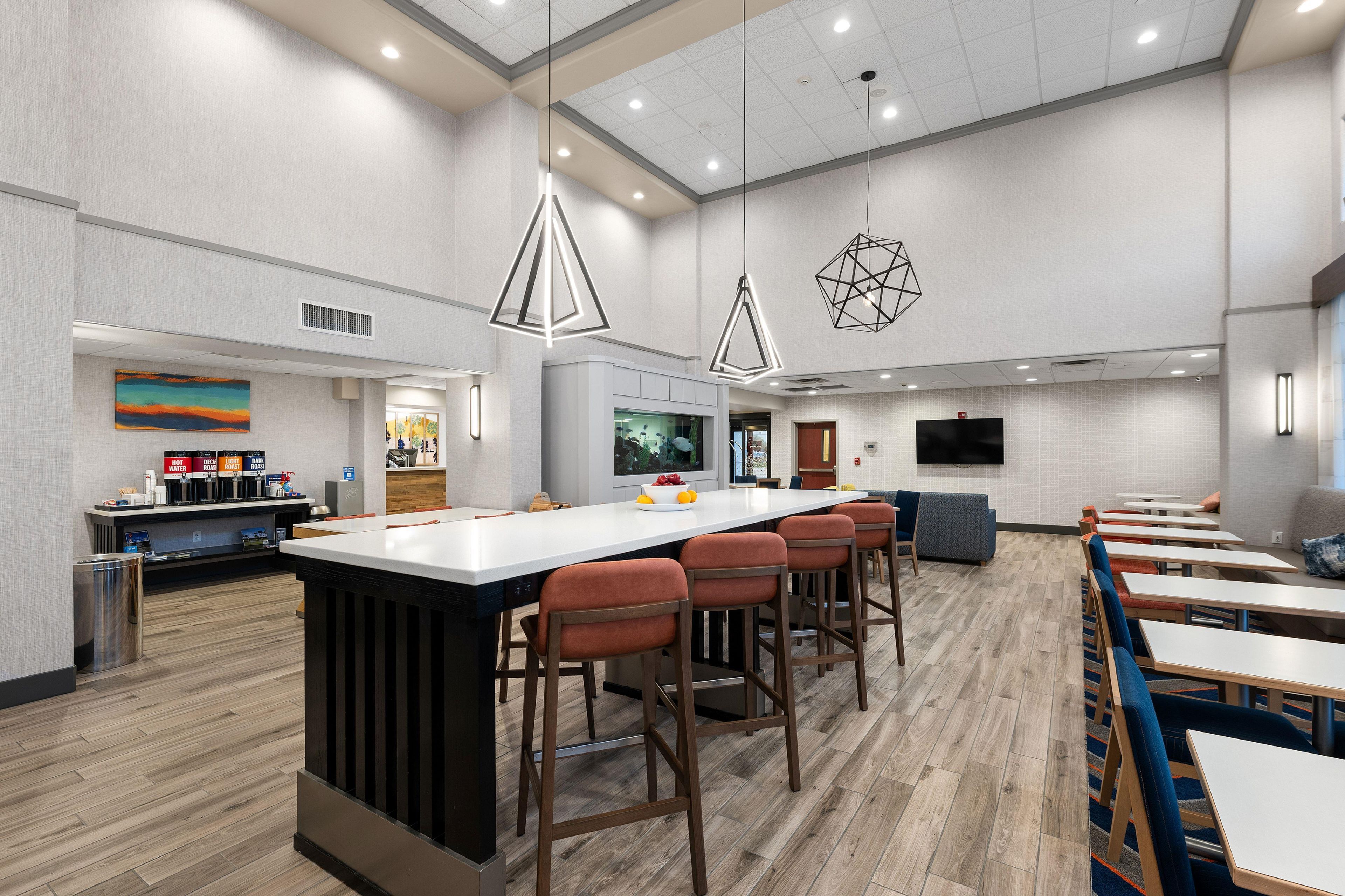 A modern kitchen area with a central island, bar stools, and a seating area with tables and chairs.