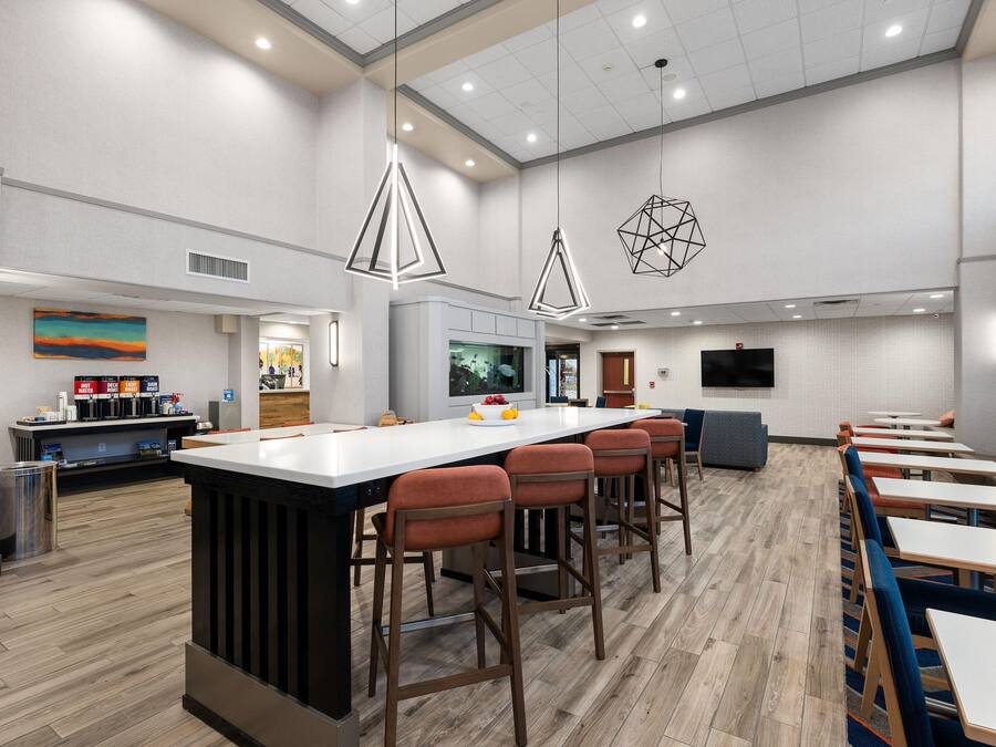 A modern kitchen area with a central island, bar stools, and a seating area with tables and chairs.