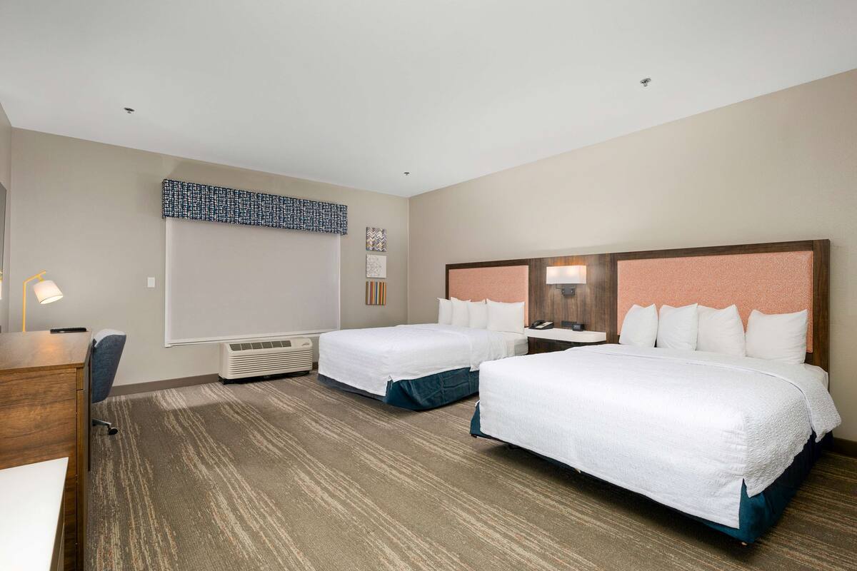 A hotel room with two beds, a desk, and a chair.