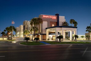 A Hampton Inn & Suites by Hilton hotel with a modern design, featuring a prominent entrance and palm trees in the landscaping.