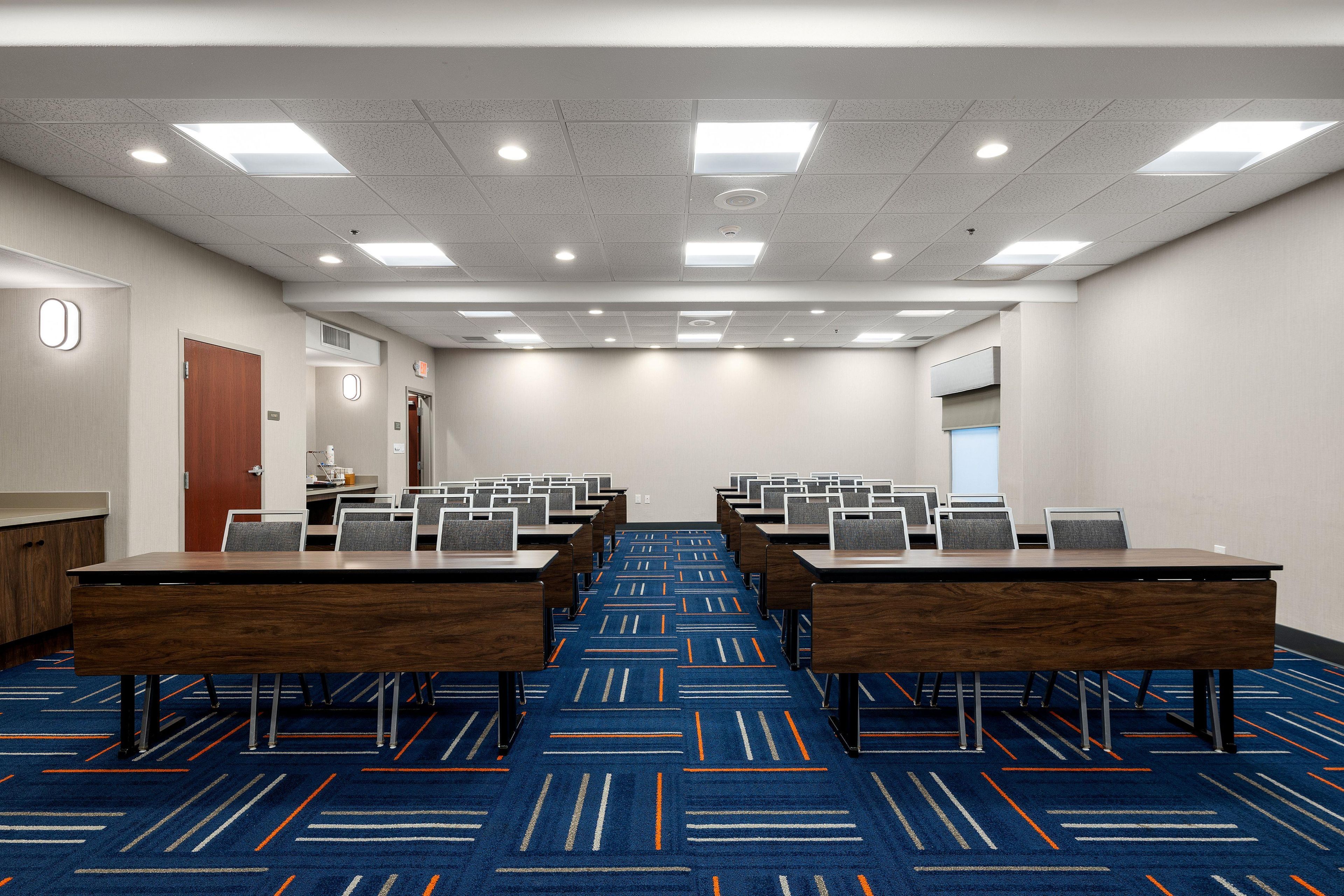 A conference room with multiple tables and chairs, a carpeted floor, and a ceiling with recessed lighting.