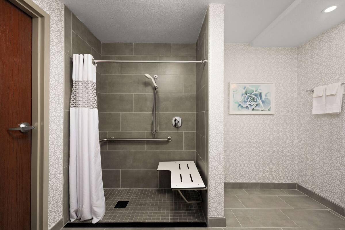 A modern bathroom with a shower, grab bar, and a small white shelf.
