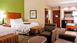 Quarto de hotel com cama, dois pufes, uma cadeira, escrivaninha e cozinha compacta.