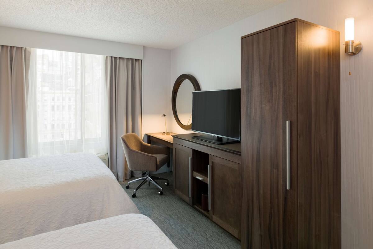 A hotel room with two beds, a desk with a television, a chair, and a wardrobe.