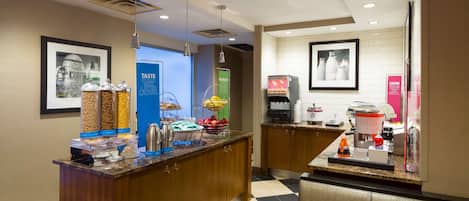 A hotel lobby with a reception desk, a coffee machine, and a food display with various snacks.
