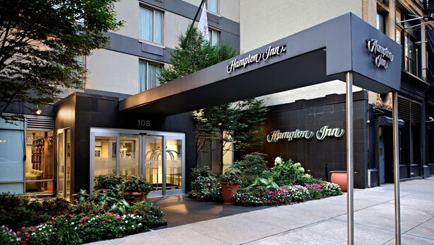 The exterior of a Hampton Inn hotel with a modern facade, large windows, and a well-maintained garden area. - Hampton Inn Manhattan-Chelsea (New York)