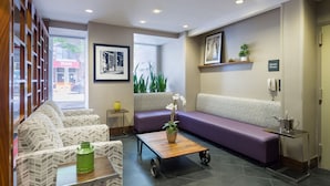 A reception area with a sofa, chairs, a coffee table, and a sign indicating a phone. - Hampton Inn Manhattan-Chelsea (New York)