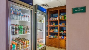 Et tekøkken med et køleskab fyldt med drikkevarer og snacks, en fryser samt et træskab med emballerede fødevarer.