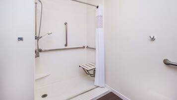 A wheelchair-accessible shower with grab bars, a white shower curtain, and a small shelf.