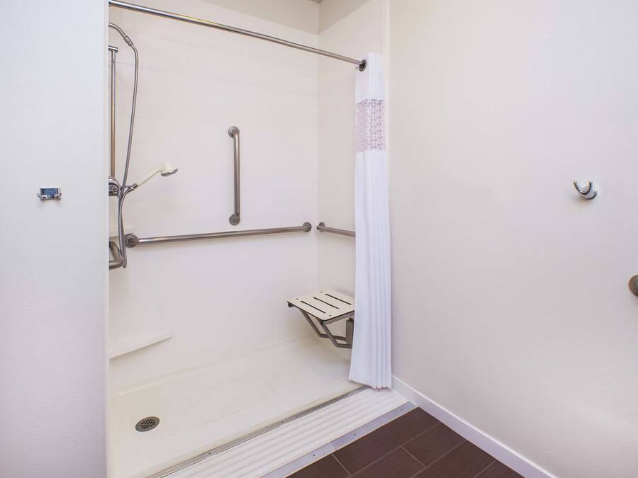 A wheelchair-accessible shower with grab bars, a white shower curtain, and a small shelf.