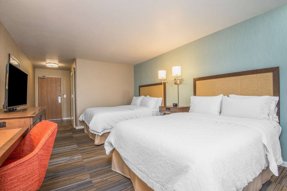 A hotel room with two beds, a desk with a TV, and a red chair.