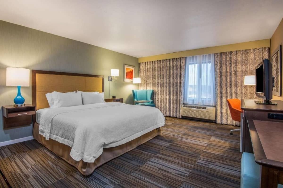 A hotel room with a large bed, a desk, a chair, a TV, and a window with curtains.