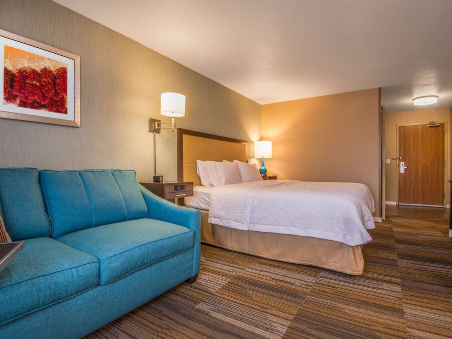 A hotel room with a bed, a blue sofa, a nightstand with a lamp, and a framed picture on the wall.