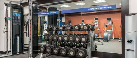 Un gimnasio con equipo de ejercicio, pesas y un dispensador de agua.