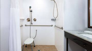 A bathroom with white tiled walls, a shower with a handheld showerhead, a grab bar, and a white pedestal sink.