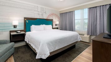 A hotel room with a large bed, a desk, a chair, a nightstand, a lamp, and a window with curtains.
