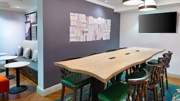 A conference room with a large table, green chairs, and a wall-mounted TV.