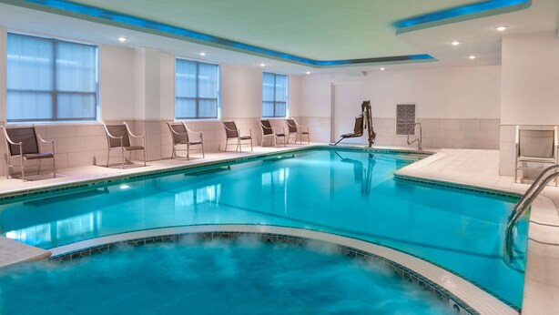 Een groot overdekt zwembad met helderblauw water, omringd door ligbedden en een sauna.