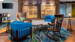Een moderne zithoek met blauwe fauteuils, een houten schommelstoel, een ronde tafel en een vloerkleed met dessin.
