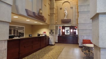 A hotel lobby with a reception desk, a statue, and a patterned carpet.