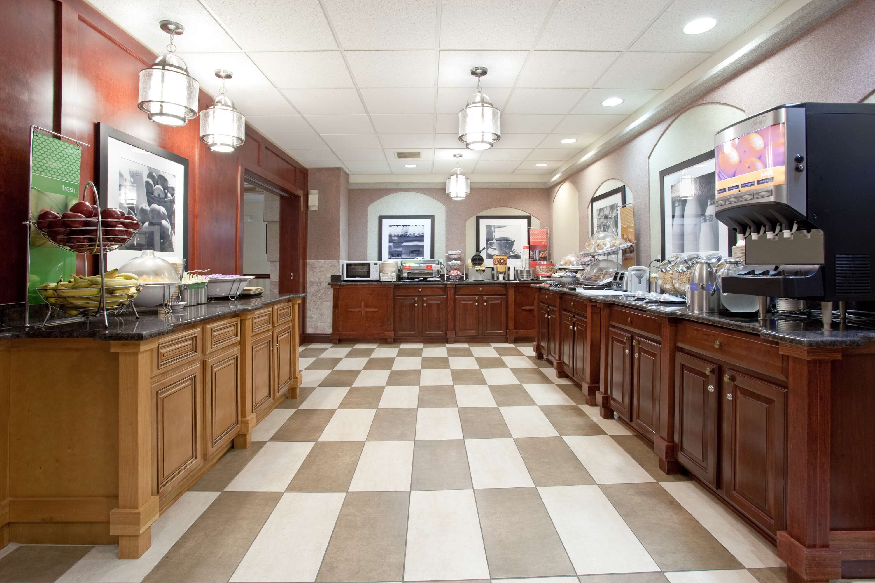 A hotel kitchen with checkered flooring, wooden cabinets, a coffee machine, and various food items on display.