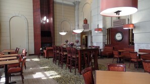 A spacious hotel lobby with multiple dining tables and chairs, a large clock on the wall, and a patterned carpet. - Hampton Inn Bowling Green (Bowling Green)