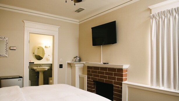 A hotel room with a large bed, a fireplace, a television mounted on the wall, and a bathroom with a sink and mirror.