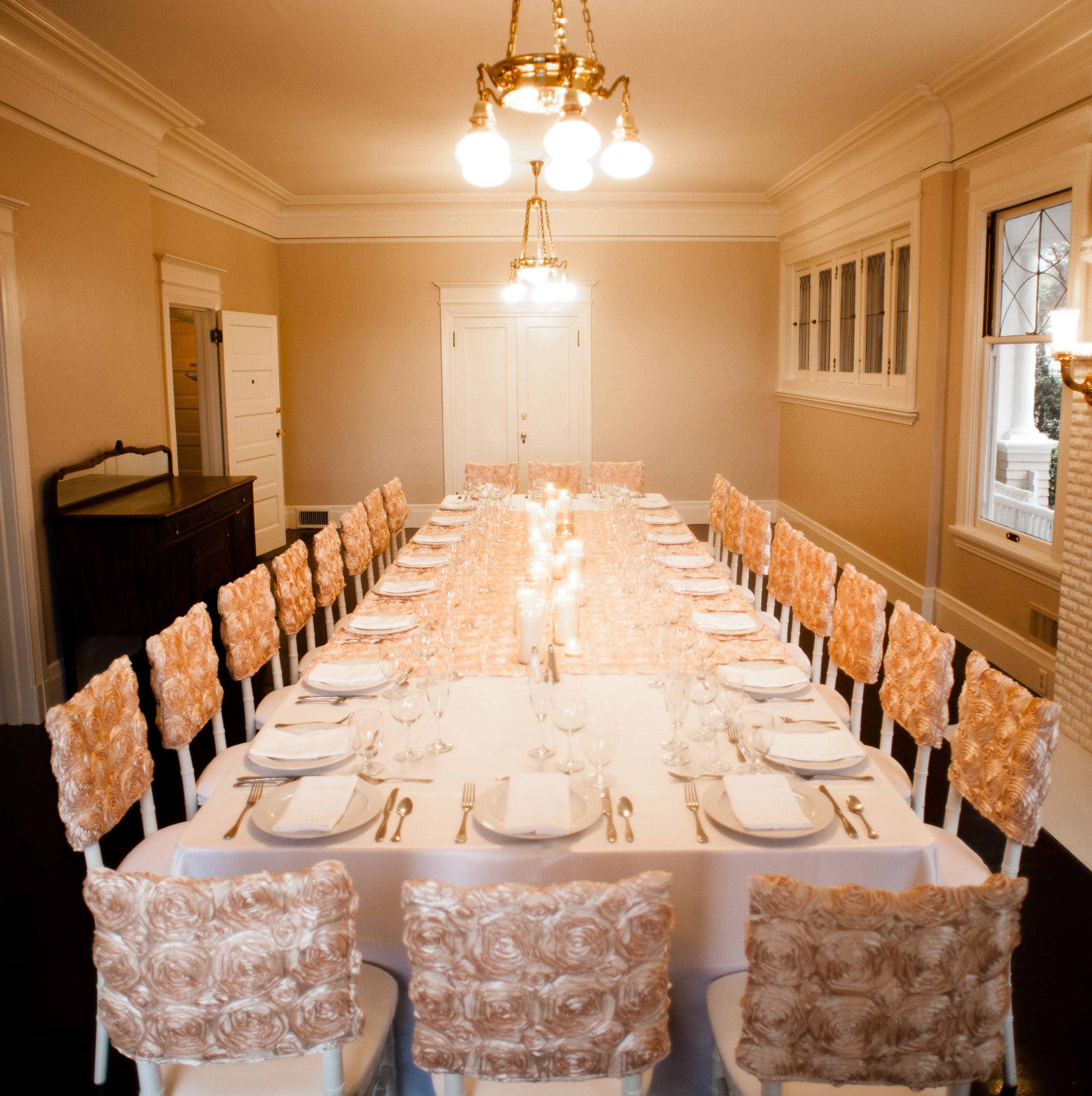A long dining table set for a formal event with chairs upholstered in a floral pattern.