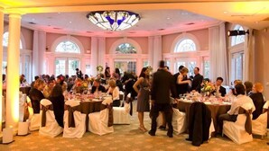 A formal event in a spacious hall with round tables, white drapery, and a large chandelier. - Vizcaya (Sacramento)