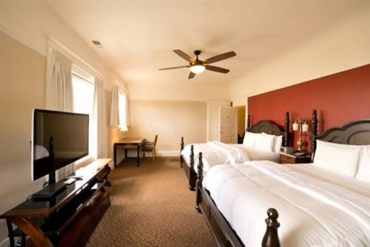 A hotel room with a bed, a desk, a television, and a ceiling fan.