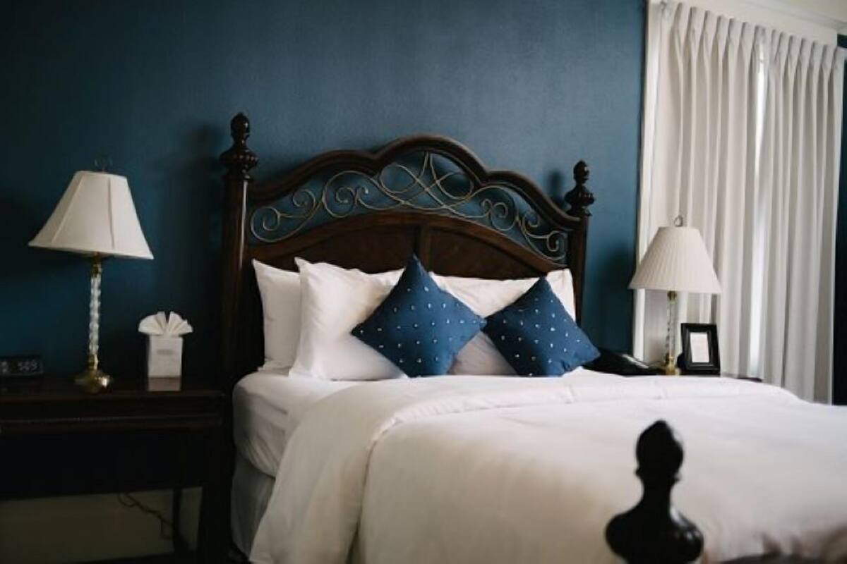A neatly made bed with white bedding and blue pillows, a wooden headboard, a bedside table with a lamp, and a nightstand with a lamp and a tissue box.