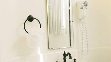 Un baño con lavamanos blanco, grifos negros, un espejo y dos apliques de pared.