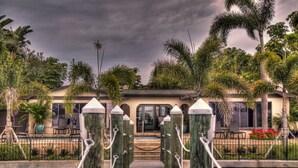 A pathway leading to a building with a pool, surrounded by palm trees and a cloudy sky. - Pasa Tiempo Private Waterfront Resort - Adults Only (St. Pete Beach)