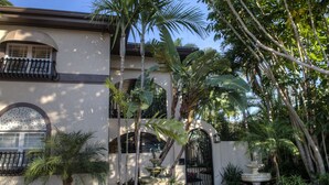 A courtyard with a fountain, palm trees, and a building with arched windows and a balcony. - Pasa Tiempo Private Waterfront Resort - Adults Only (St. Pete Beach)