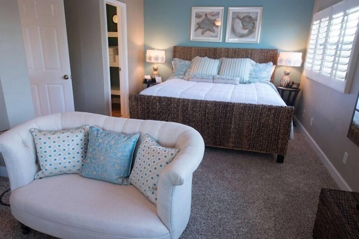 A bedroom with a large bed, a white armchair, and two wall-mounted lamps.