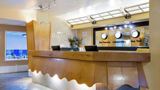 Un mostrador de recepción de hotel con diseño de madera, un reloj y un cartel que menciona San Francisco, Lawrenceburg y Nueva York.